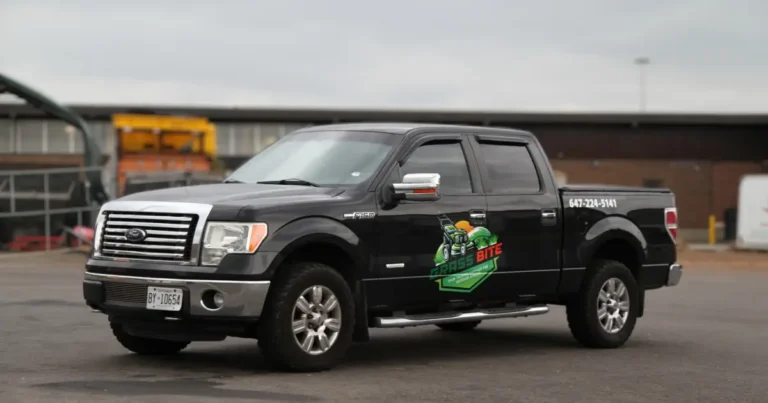 A 2014 Ford F-150 Super Cab truck captured in an angled side view, displaying Grass Bite company decals